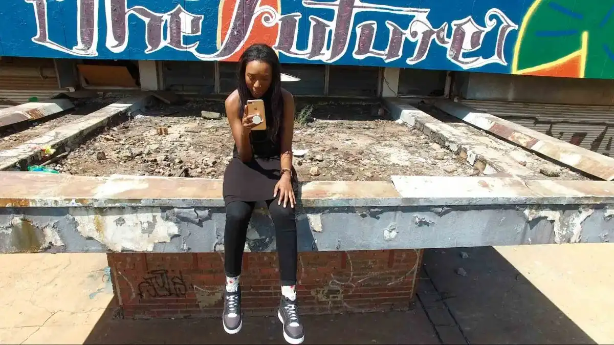 Woman sitting on a ledge, looking at her phone, with graffiti art reading "The Future" in the background.