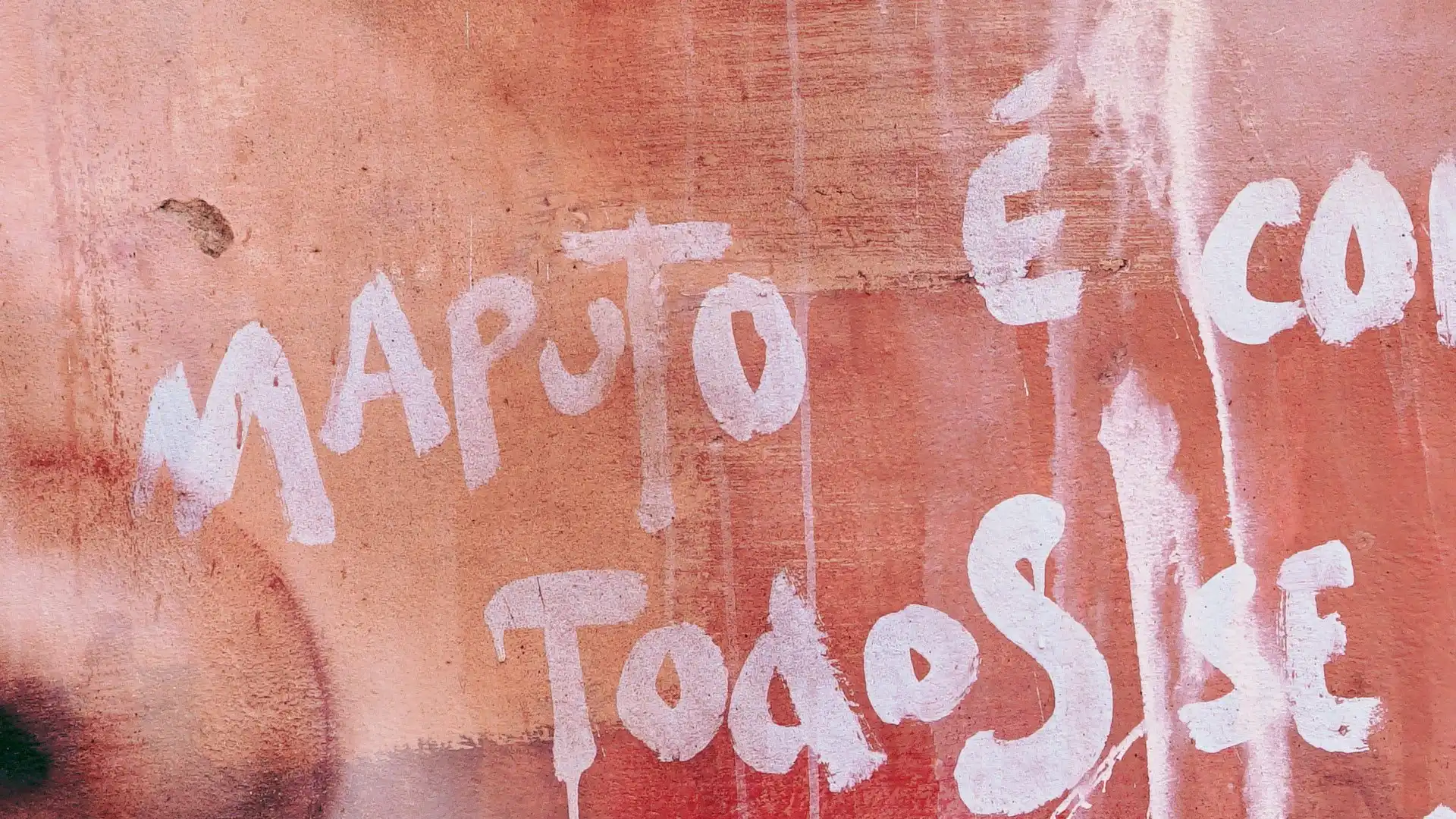 Graffiti on a textured wall with the words "Maputo é com todos" in white paint.