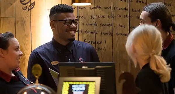 Group of Nando's staff smiling and chatting at the counter in a warmly lit restaurant.