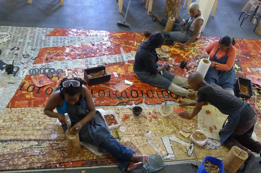 Artists collaboratively creating a colorful mosaic on a large canvas, surrounded by tools and materials.
