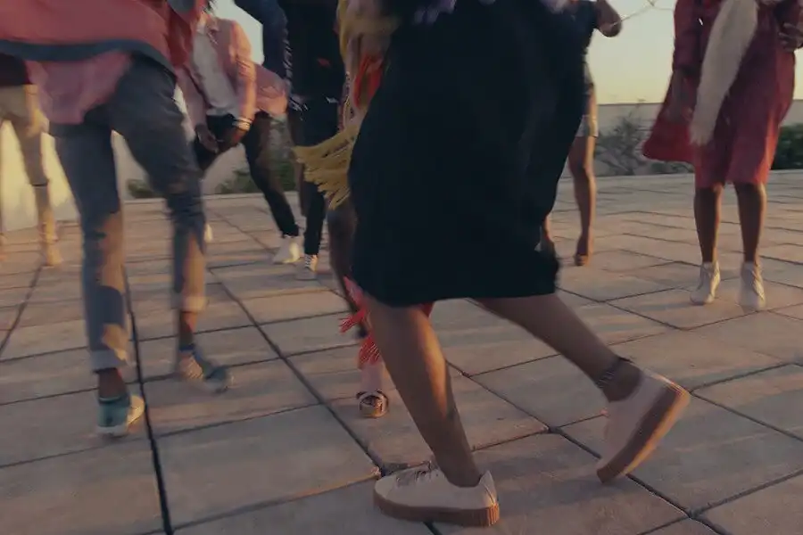 People dancing energetically on a tiled outdoor floor at sunset, with blurred motion capturing the lively atmosphere.