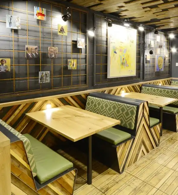 Cozy restaurant booth with wooden accents, green cushions, and artistic wall decor. Warm lighting creates an inviting atmosphere.