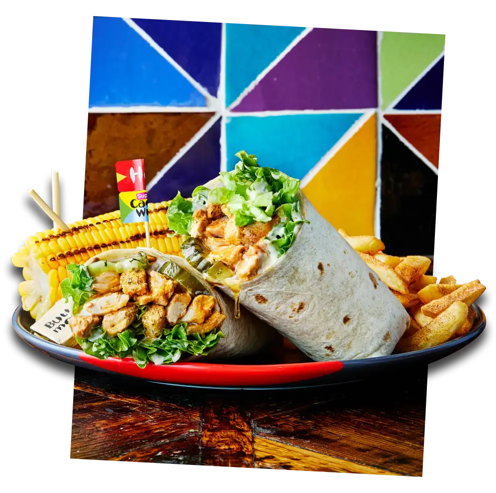 A chicken wrap with lettuce, a side of fries, corn on the cob, and a colorful geometric background.