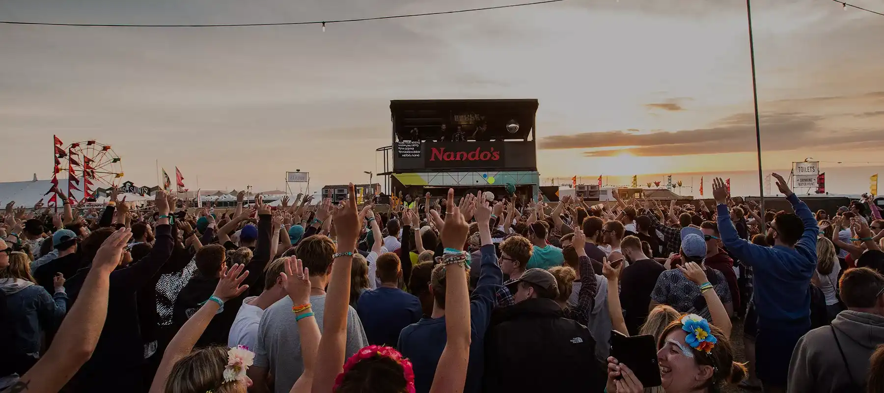 Crowd enjoying a lively outdoor event at sunset with a Nando's stall in the background.