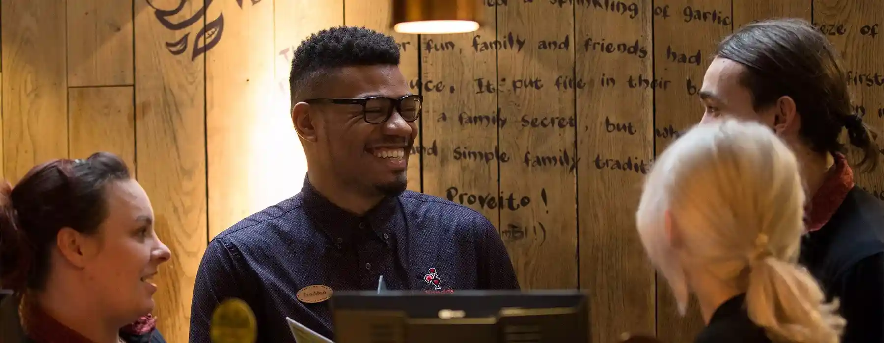 Group of people smiling and chatting at a Nando's counter, with wooden decor and warm lighting in the background.