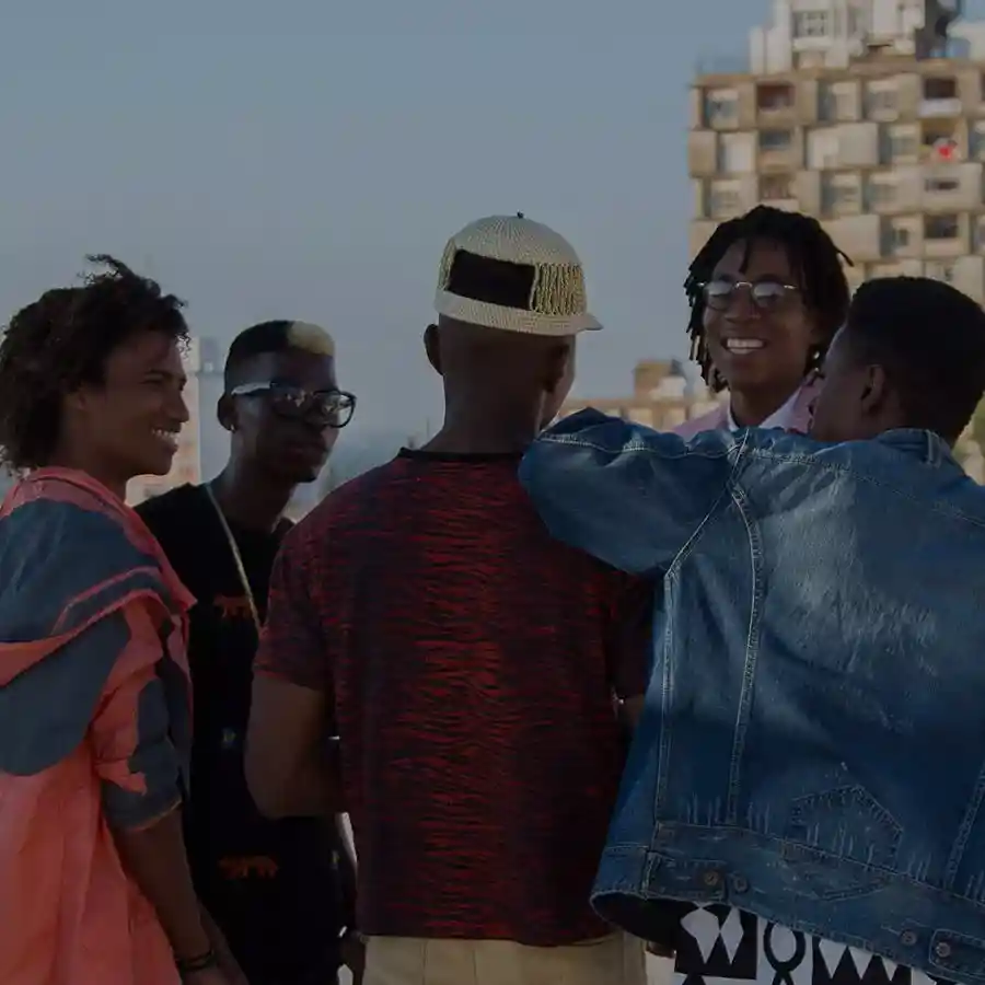 A group of five people, casually dressed, stand together outdoors, smiling and chatting under a clear sky.